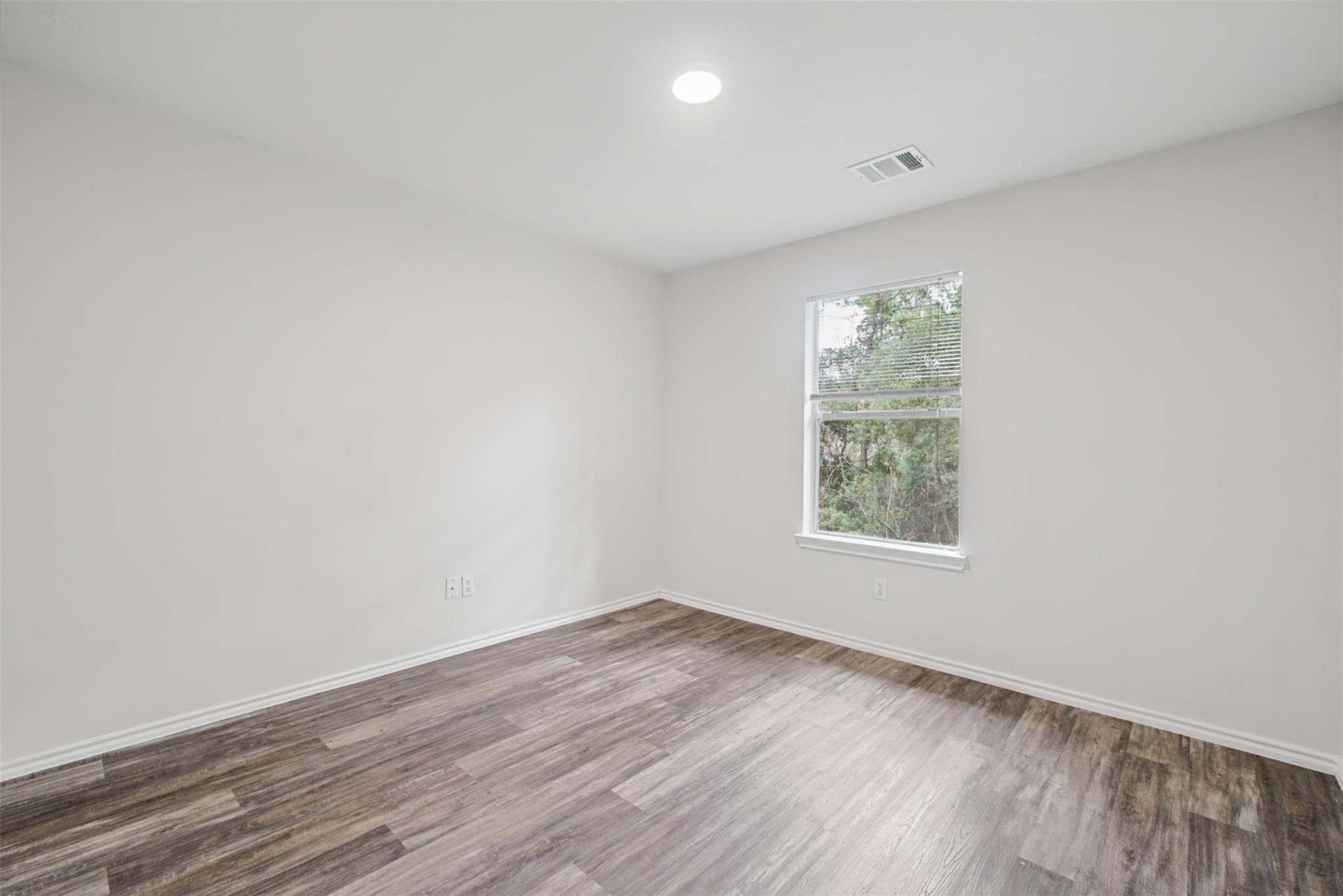 Empty room with wood-look flooring and a window overlooking trees.