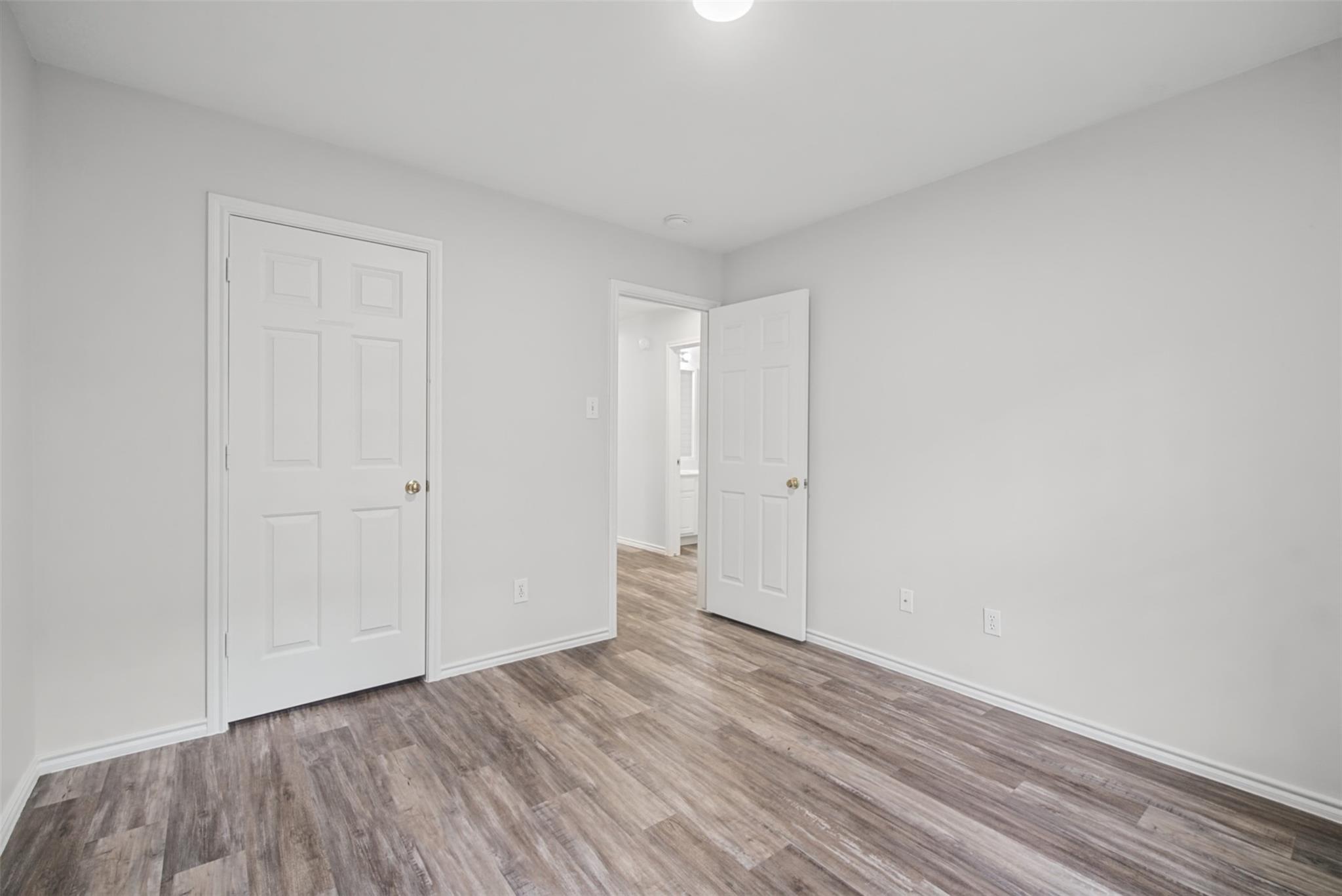 Empty room with gray-brown wood-look flooring and an open door to an adjoining area.