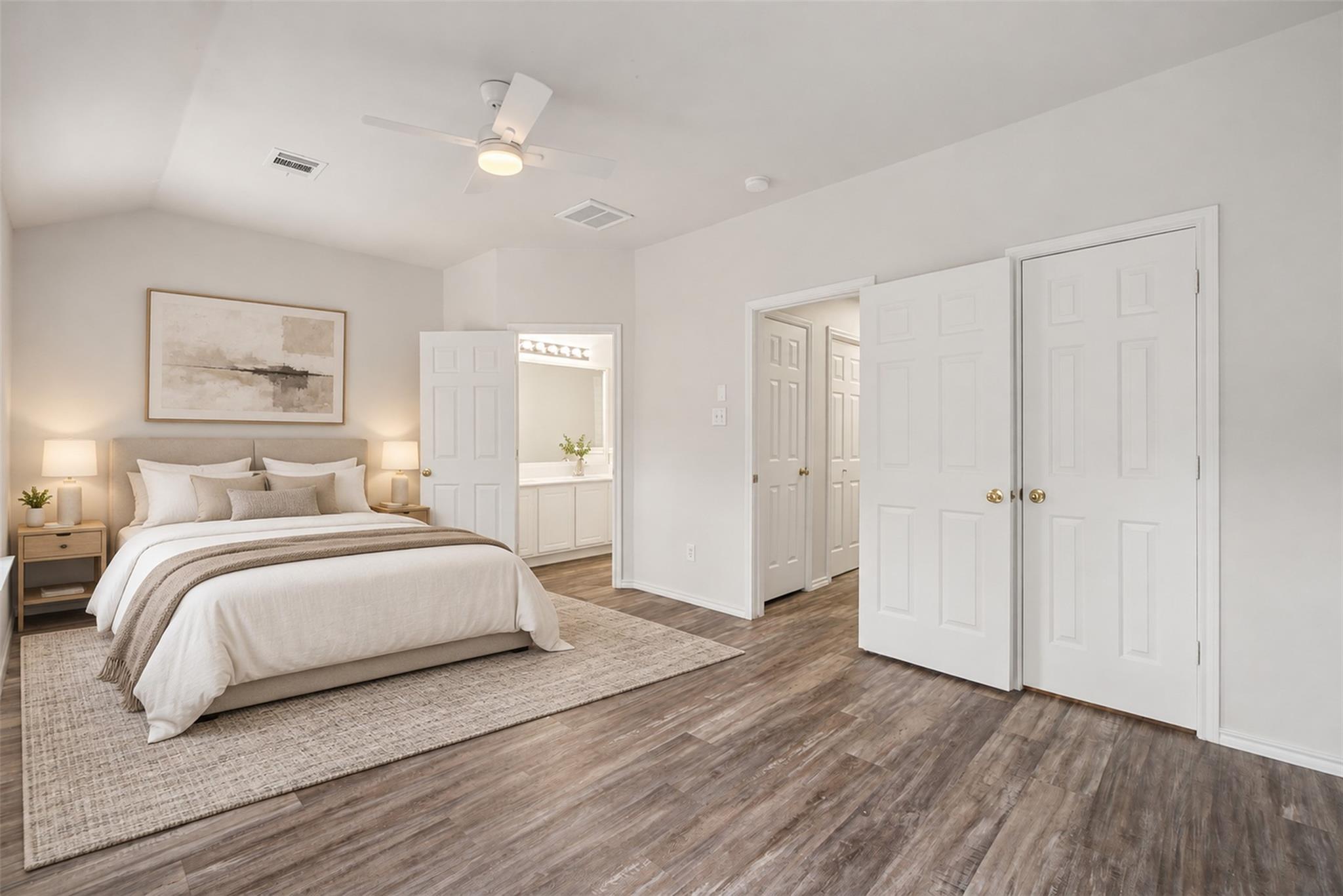 Furnished bedroom with a neutral bed, wood-look flooring, ceiling fan, and open doorway to the bathroom.