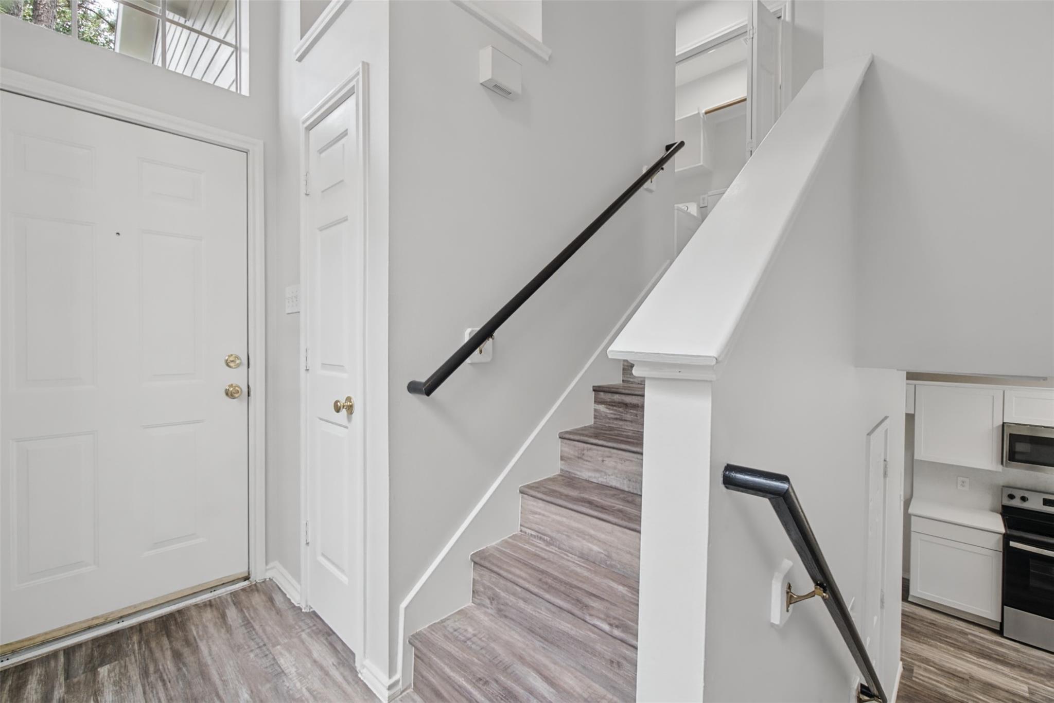 Entry foyer with gray wood-look stairs, black handrails, and a white front door.