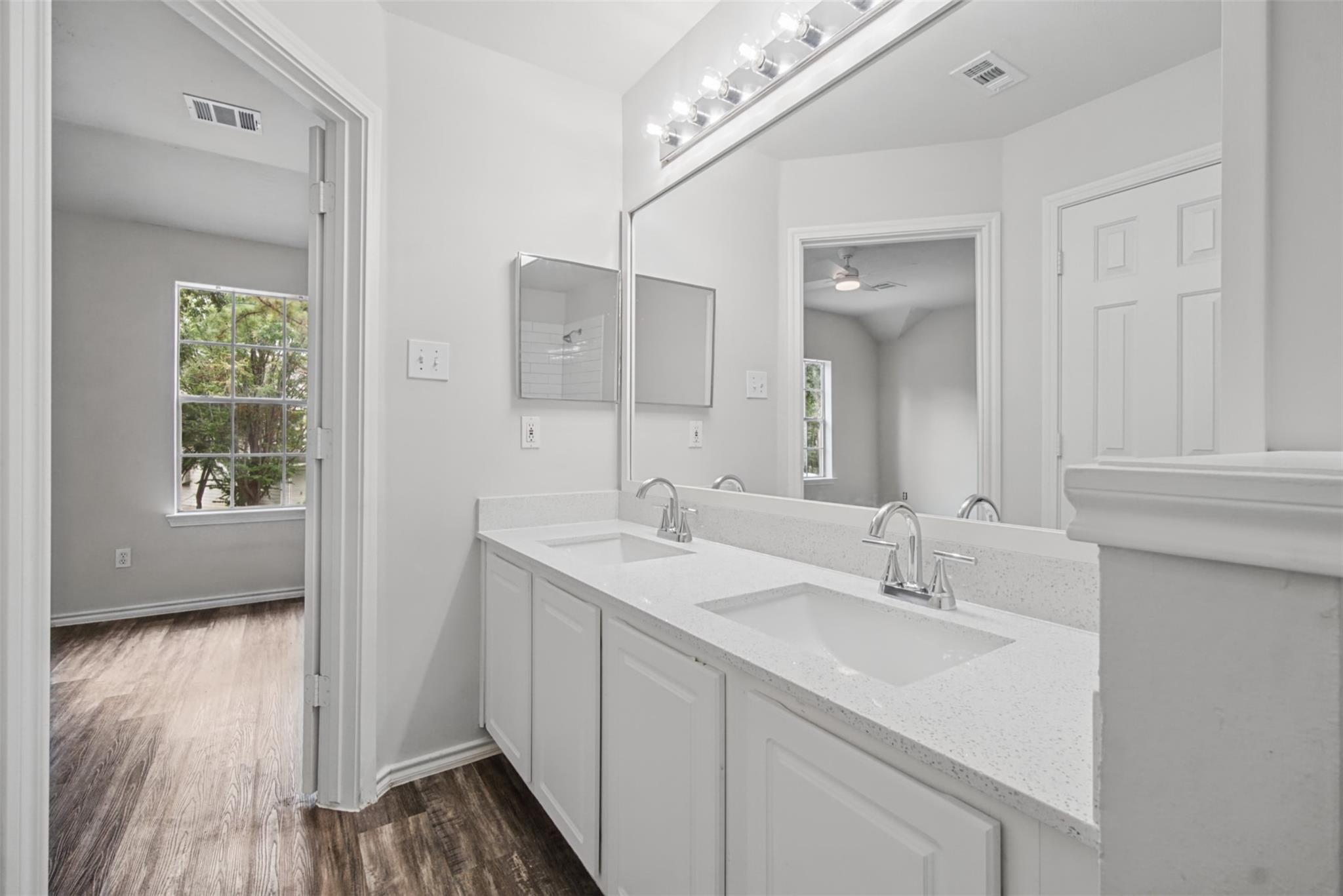Bathroom with a long double-sink vanity, large mirror, and dark wood-look flooring.