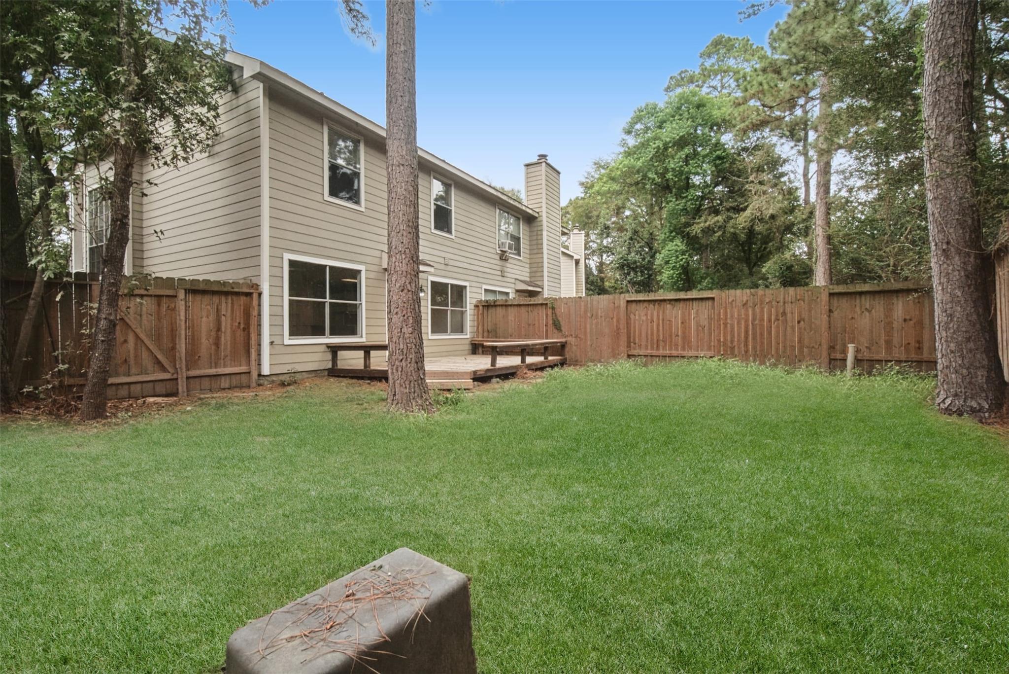 Fenced backyard with a broad lawn, mature trees, and a small deck beside the two-story home.