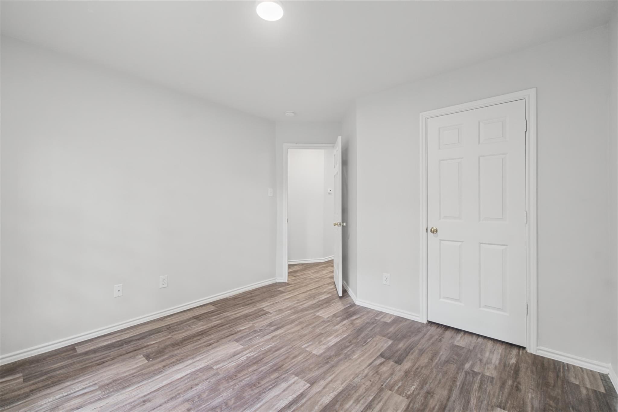 Empty room with wood-look plank flooring and an open doorway beside a closed white door.