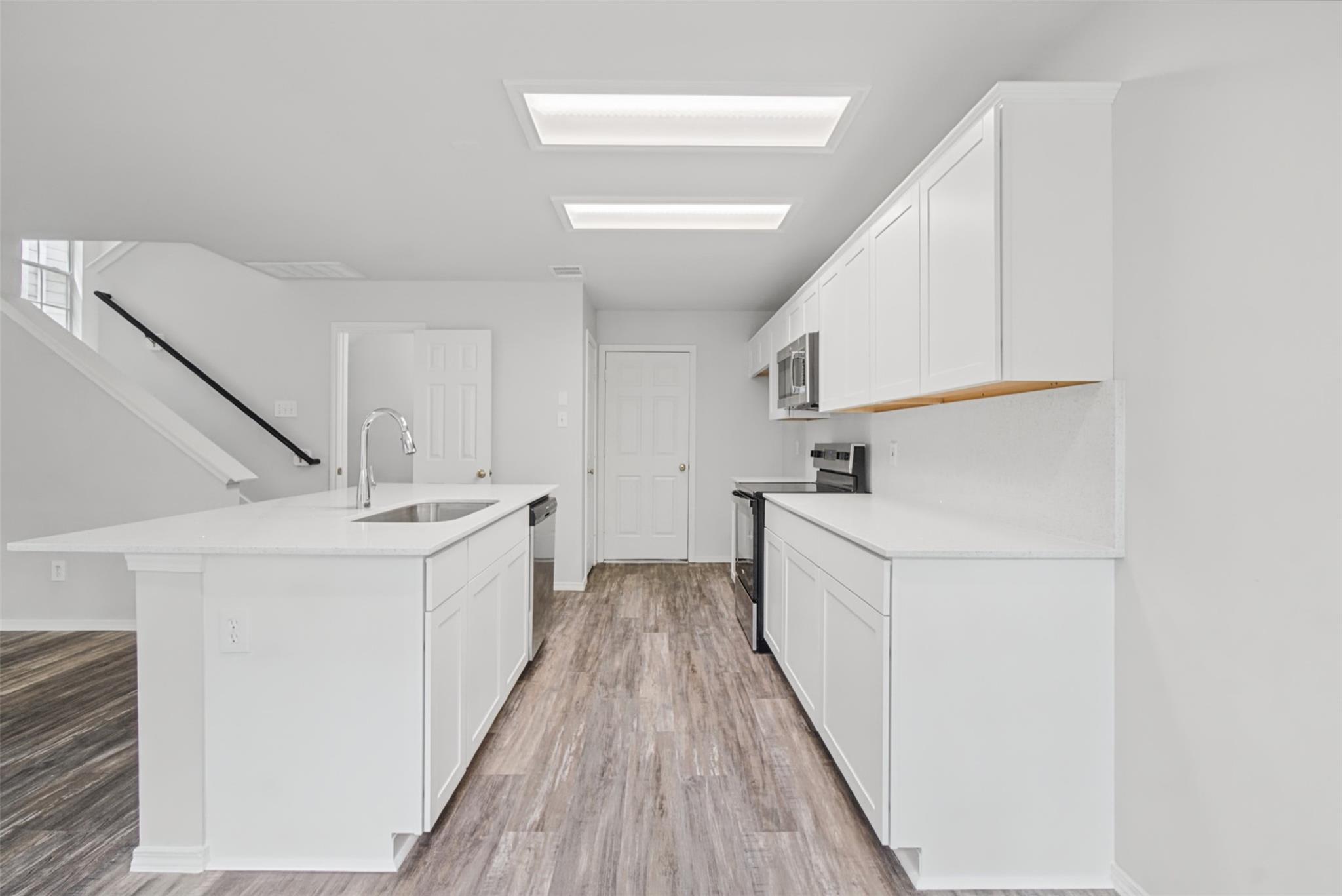 Bright kitchen with a white island, stainless steel appliances, and wood-look flooring.