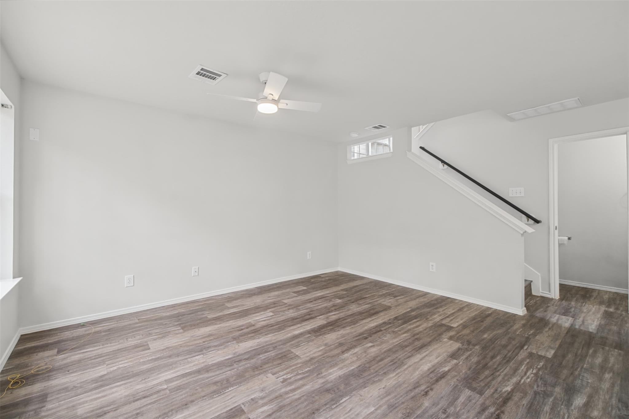 Empty room with wood-look flooring, a ceiling fan, and a staircase with a black handrail.