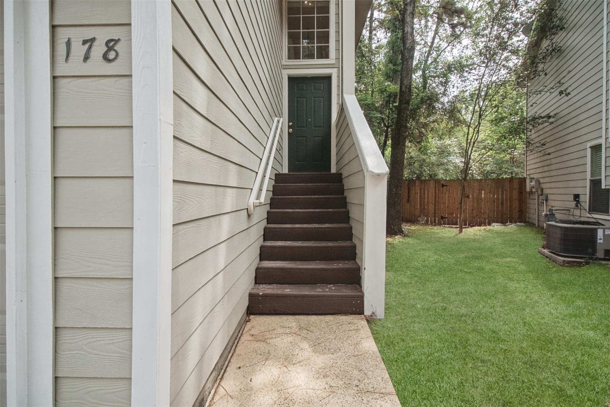Home entrance with number 178, brown steps, white railings, and a fenced lawn.