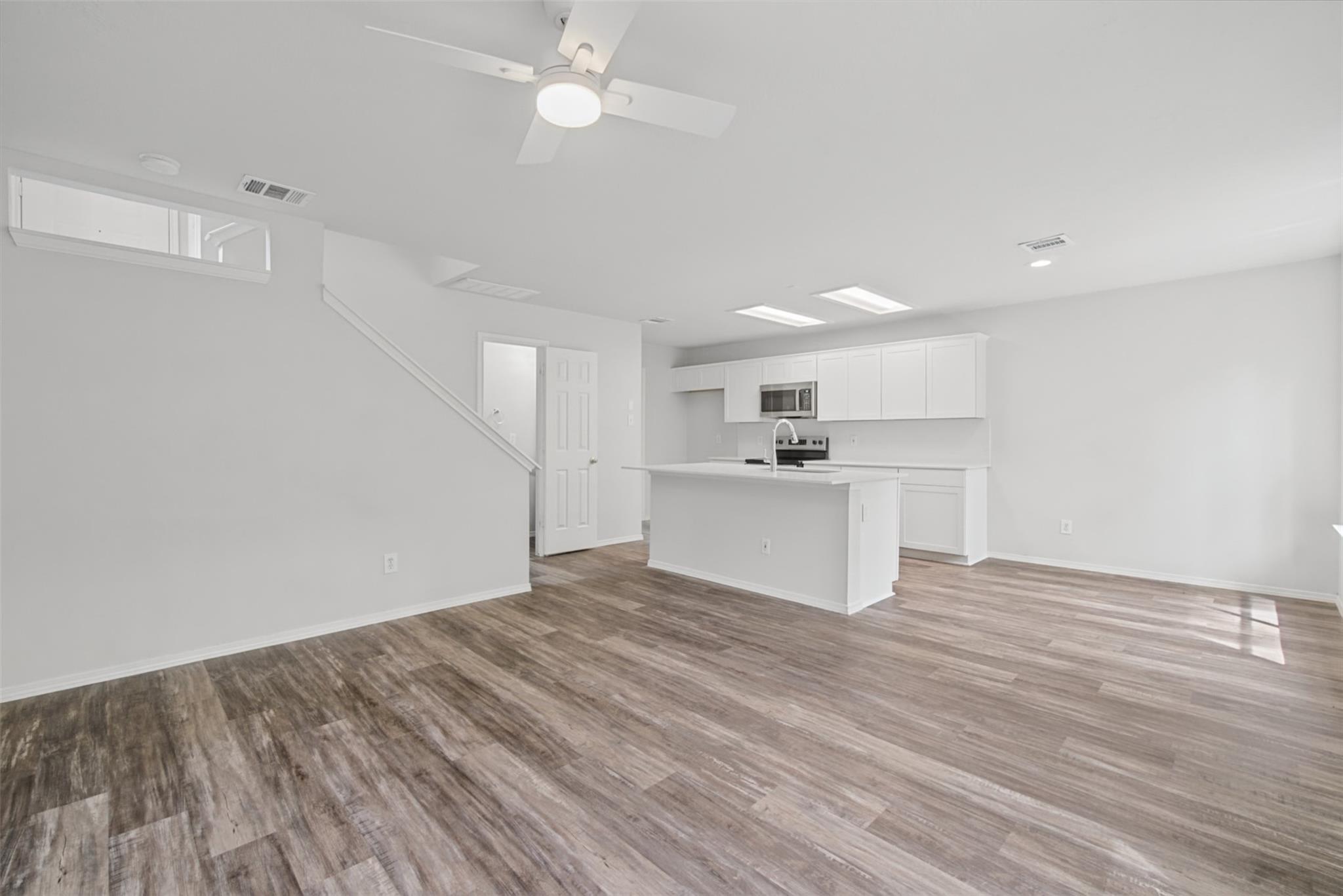 Open-plan living area and kitchen with white cabinetry, a sink peninsula, and gray wood-look flooring.
