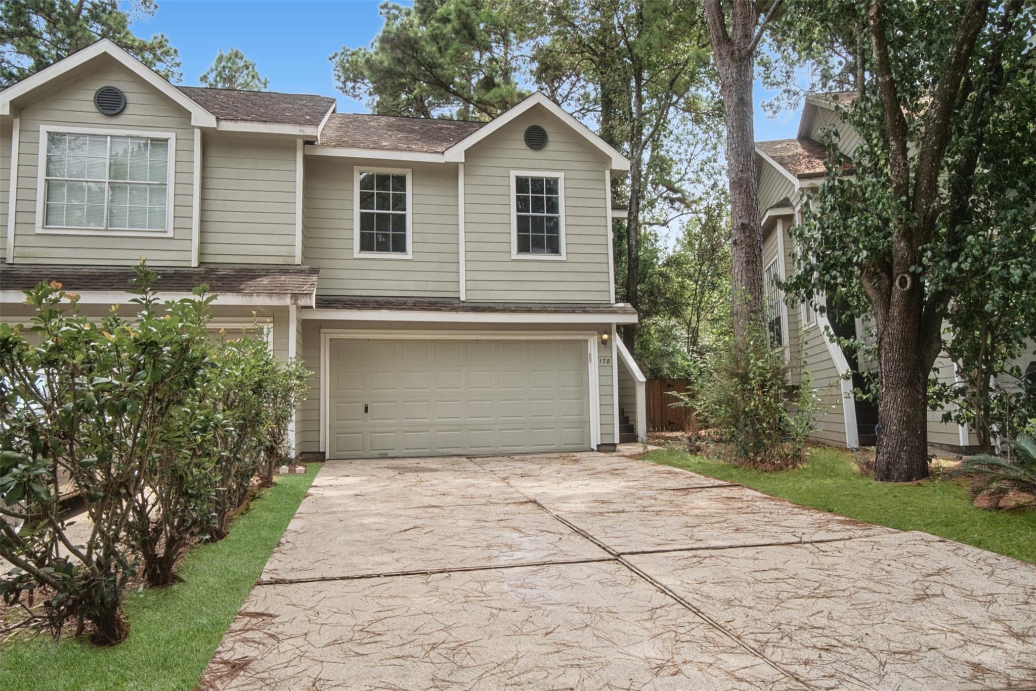 Two-story house with a double garage, broad patterned driveway, and mature trees.