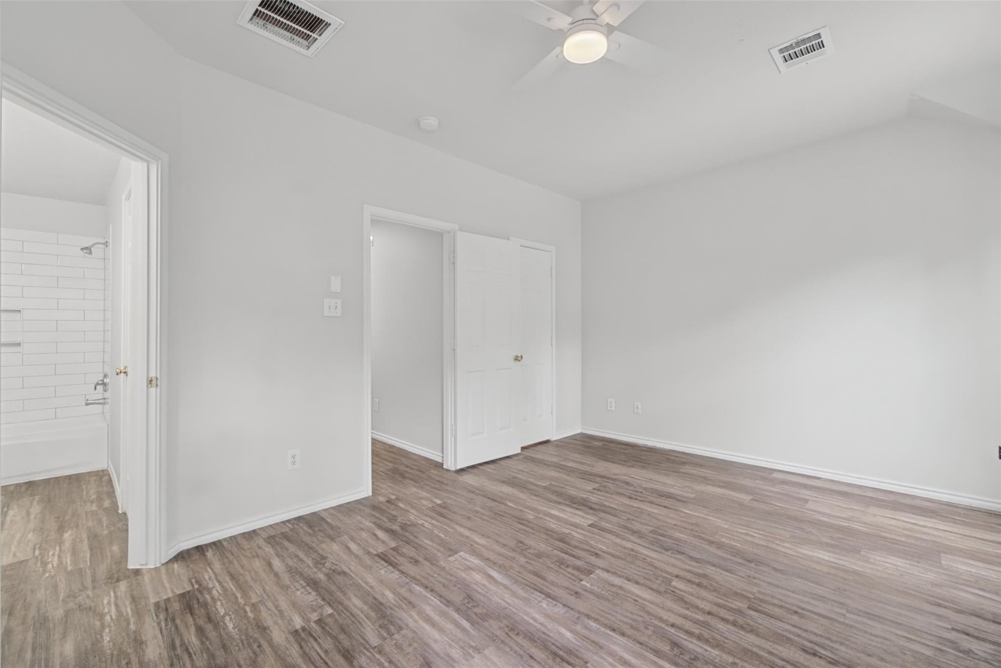 Empty bedroom with wood-look flooring, a ceiling fan, and an adjoining tiled bathroom.