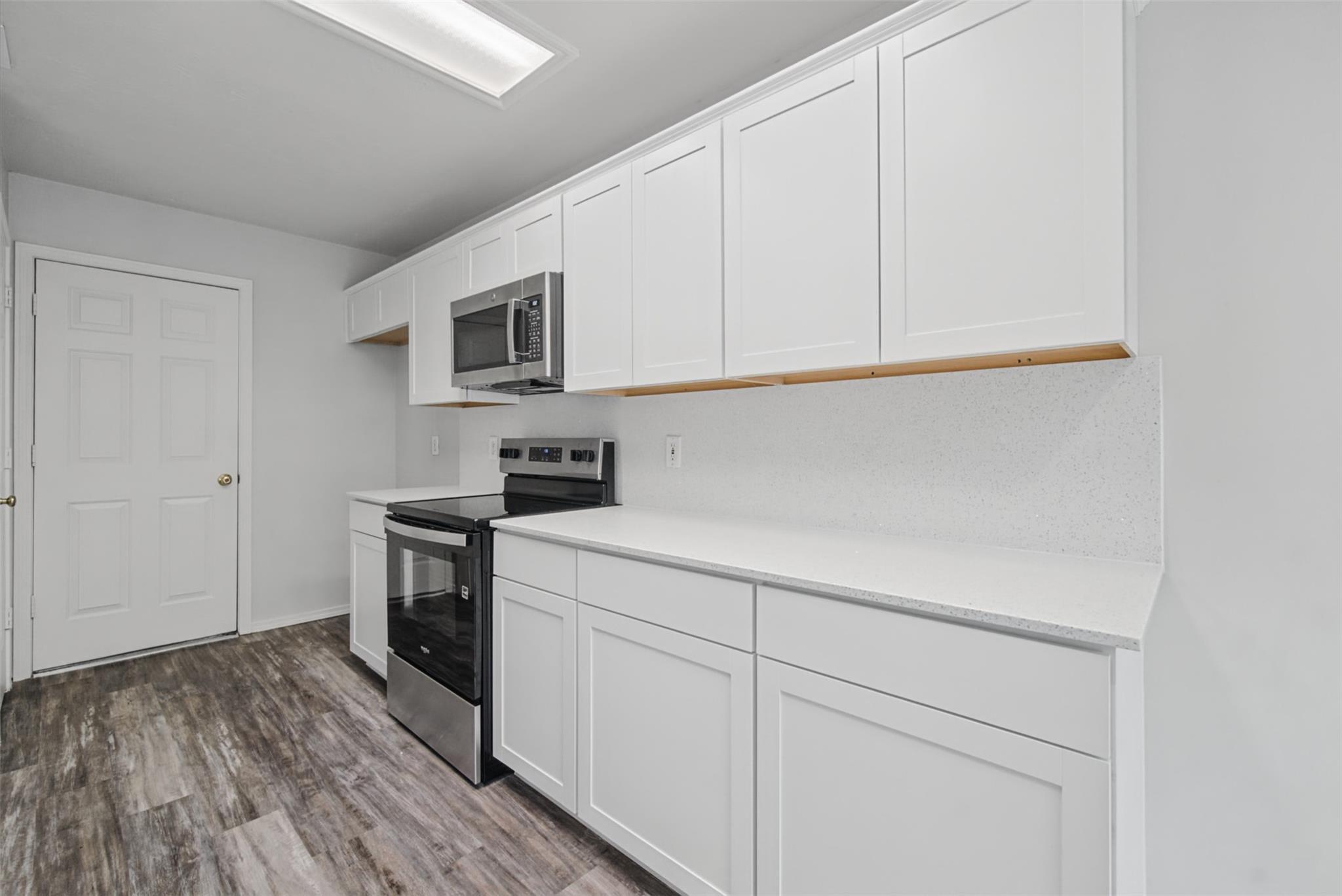 Kitchen with white shaker cabinets, stainless steel appliances, and dark wood-look flooring.