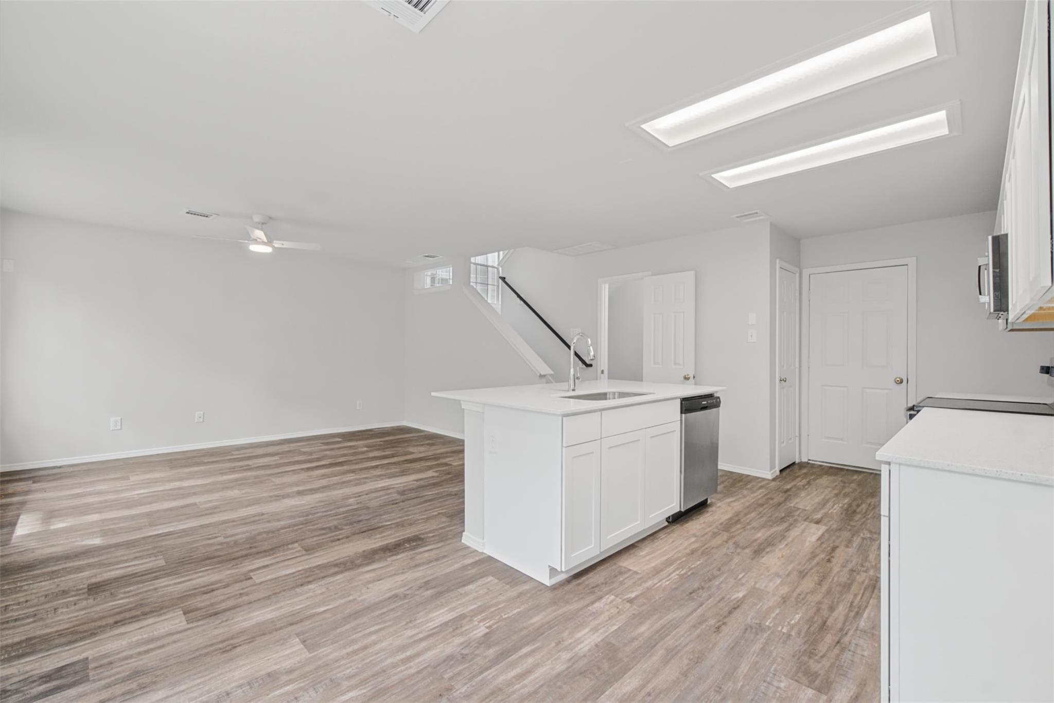 Vacant open-plan kitchen with a white island, stainless steel dishwasher, and wood-look plank flooring.