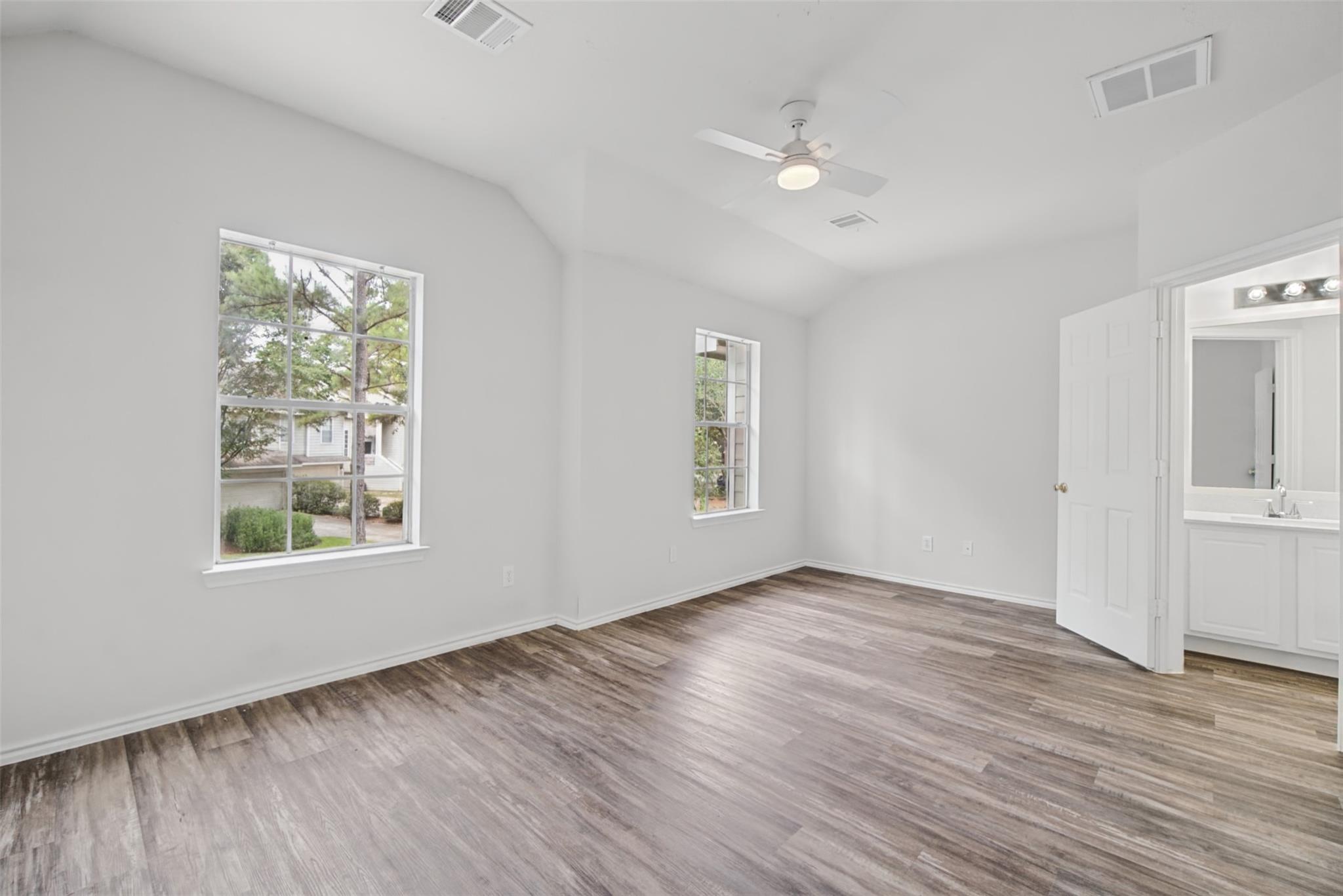 Vacant bedroom with a vaulted ceiling, wood-look flooring, and an open doorway to the bathroom.