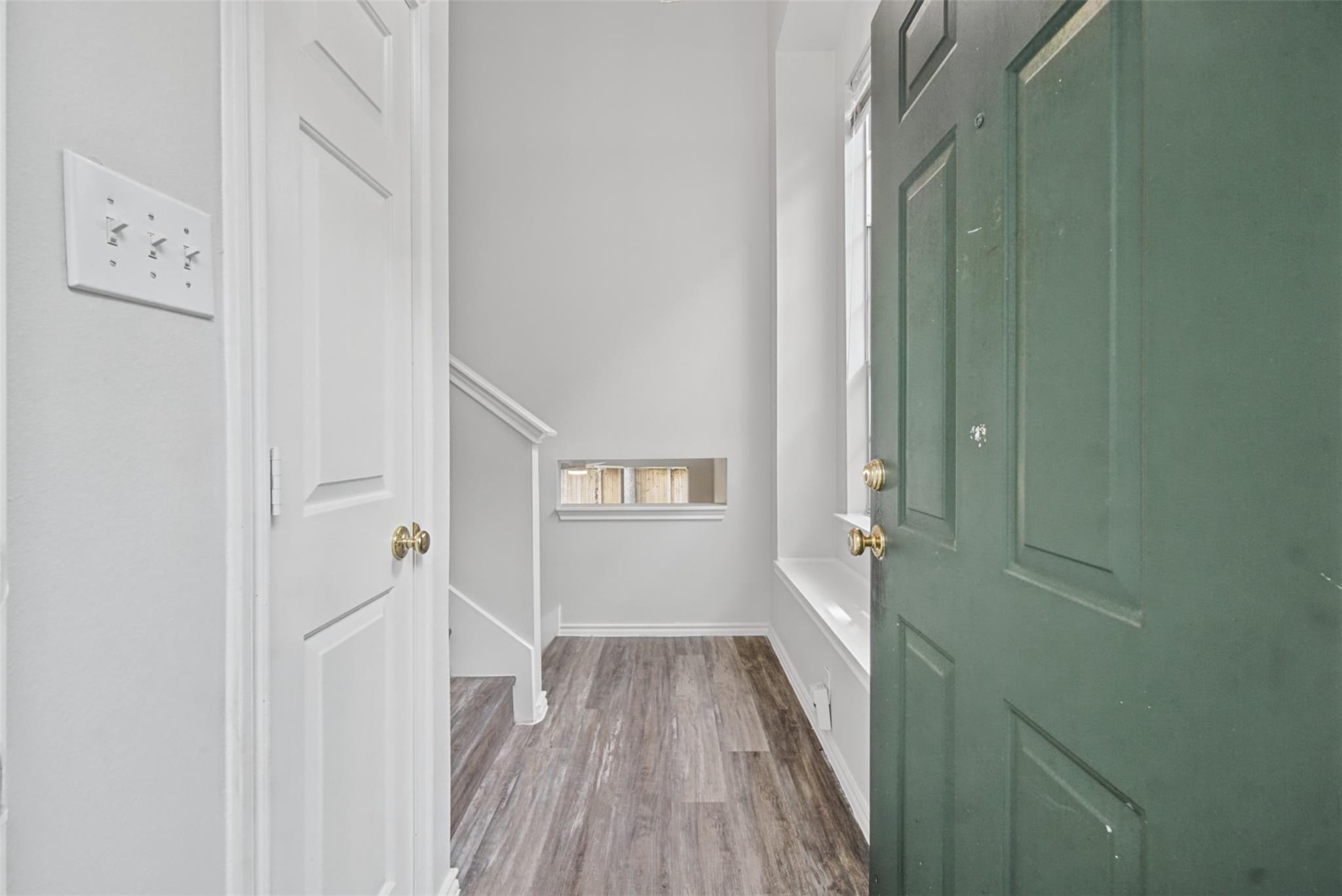 Entry hall with a dark green front door, wood-look floors, staircase, and built-in window seat.
