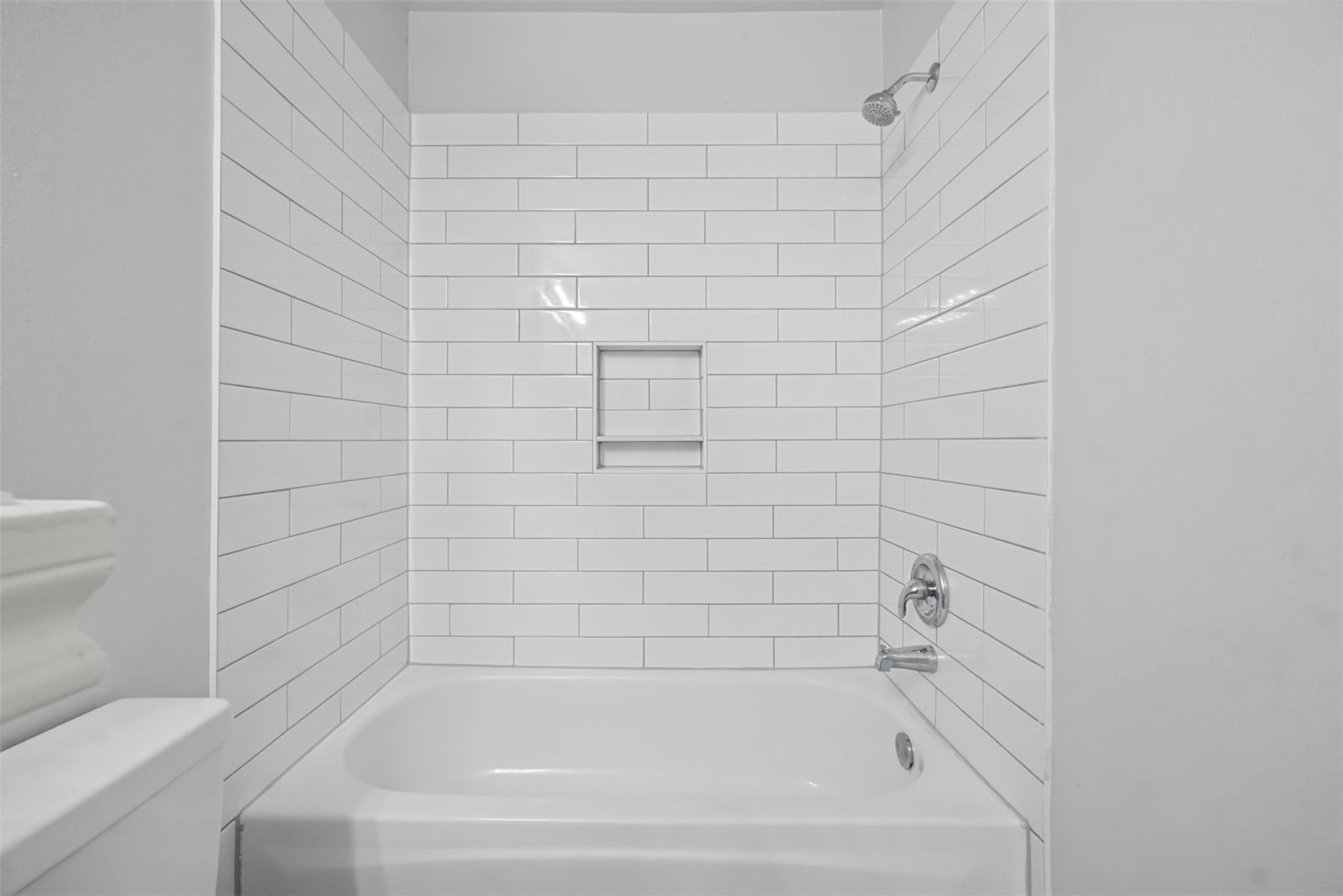 White bathtub beneath a subway-tile shower wall with a recessed niche and chrome fixtures.