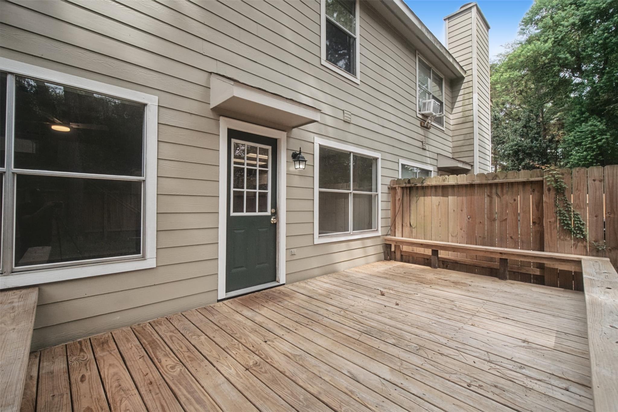 Wooden deck beside a beige two-story home, enclosed by a privacy fence with built-in bench seating.