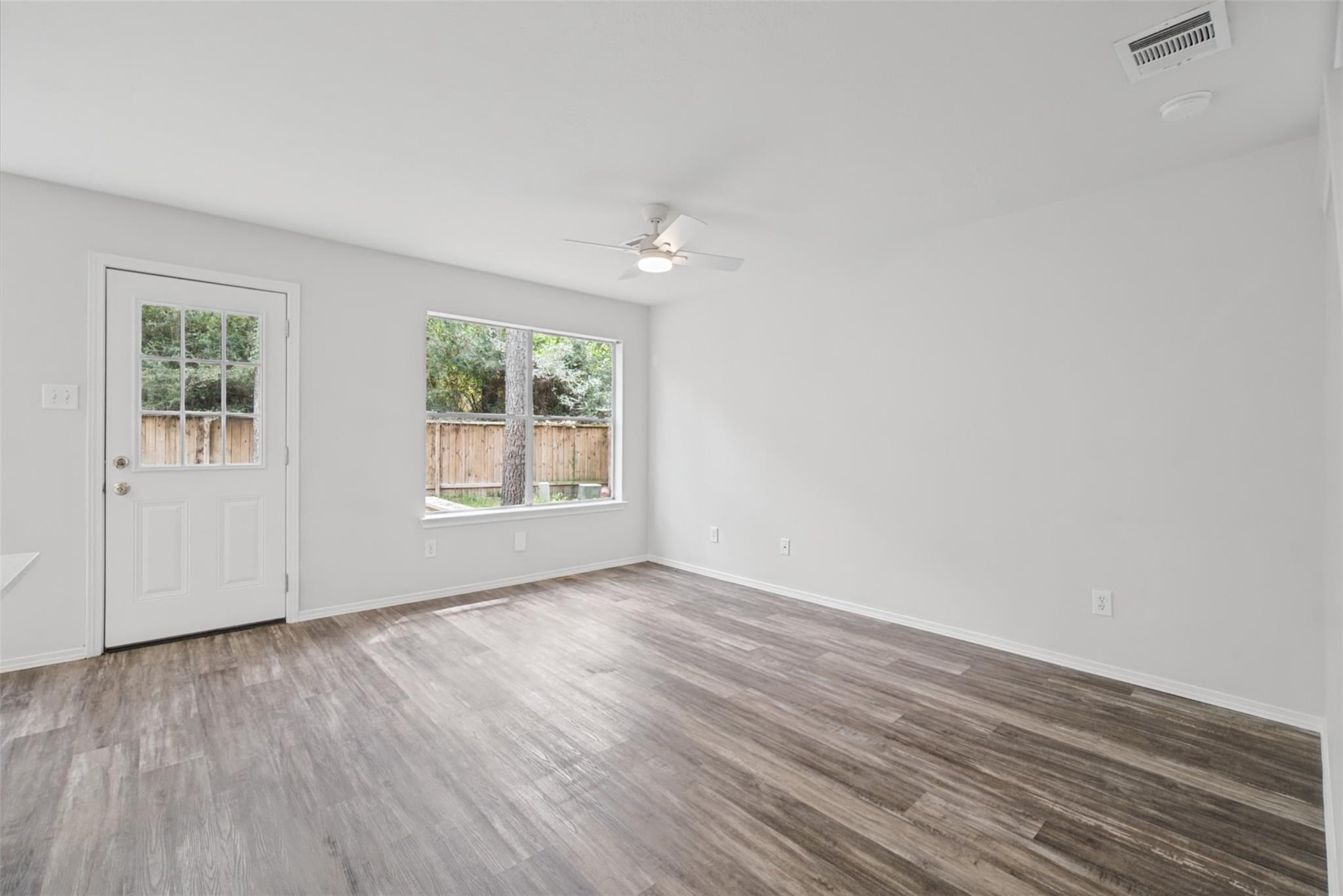 Vacant room with gray wood-look flooring, a ceiling fan, and a window facing a fenced yard.