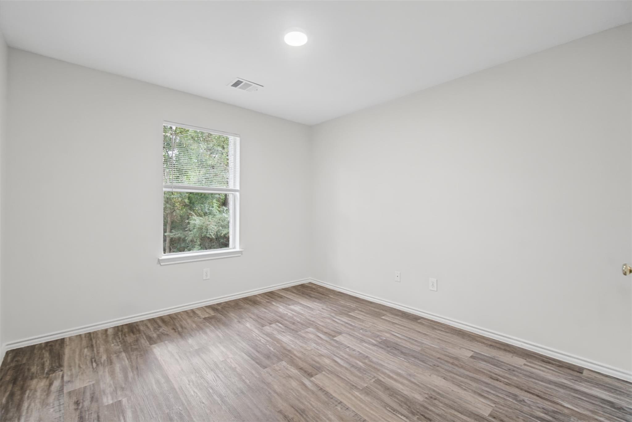 Empty room with wood-look flooring and a window overlooking trees.