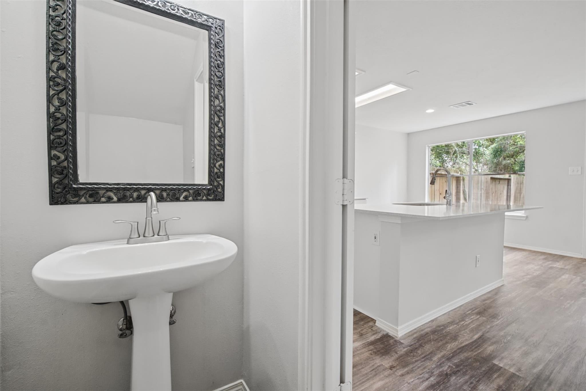 Pedestal sink and ornate mirror beside a bright kitchen with a large island.