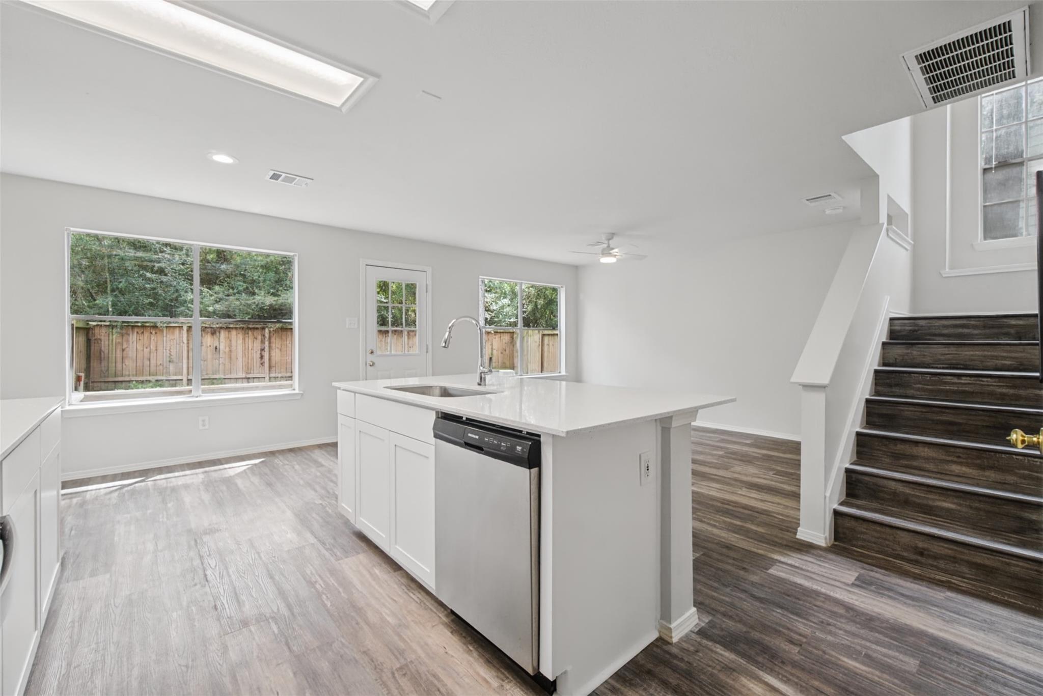 Vacant kitchen with a white island and dishwasher beside large windows and a staircase.