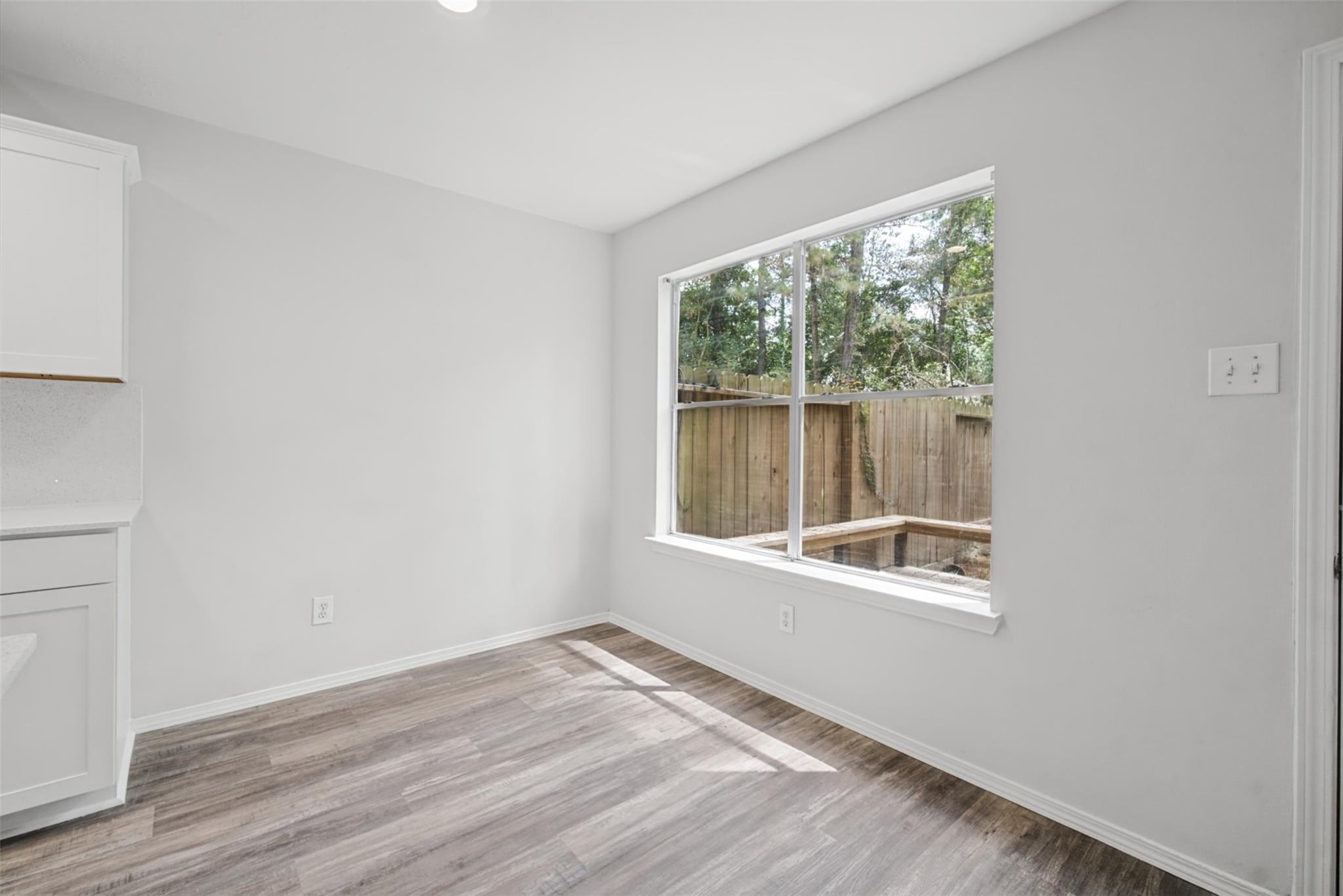 Empty kitchen nook with gray wood-look flooring and a large window overlooking trees.
