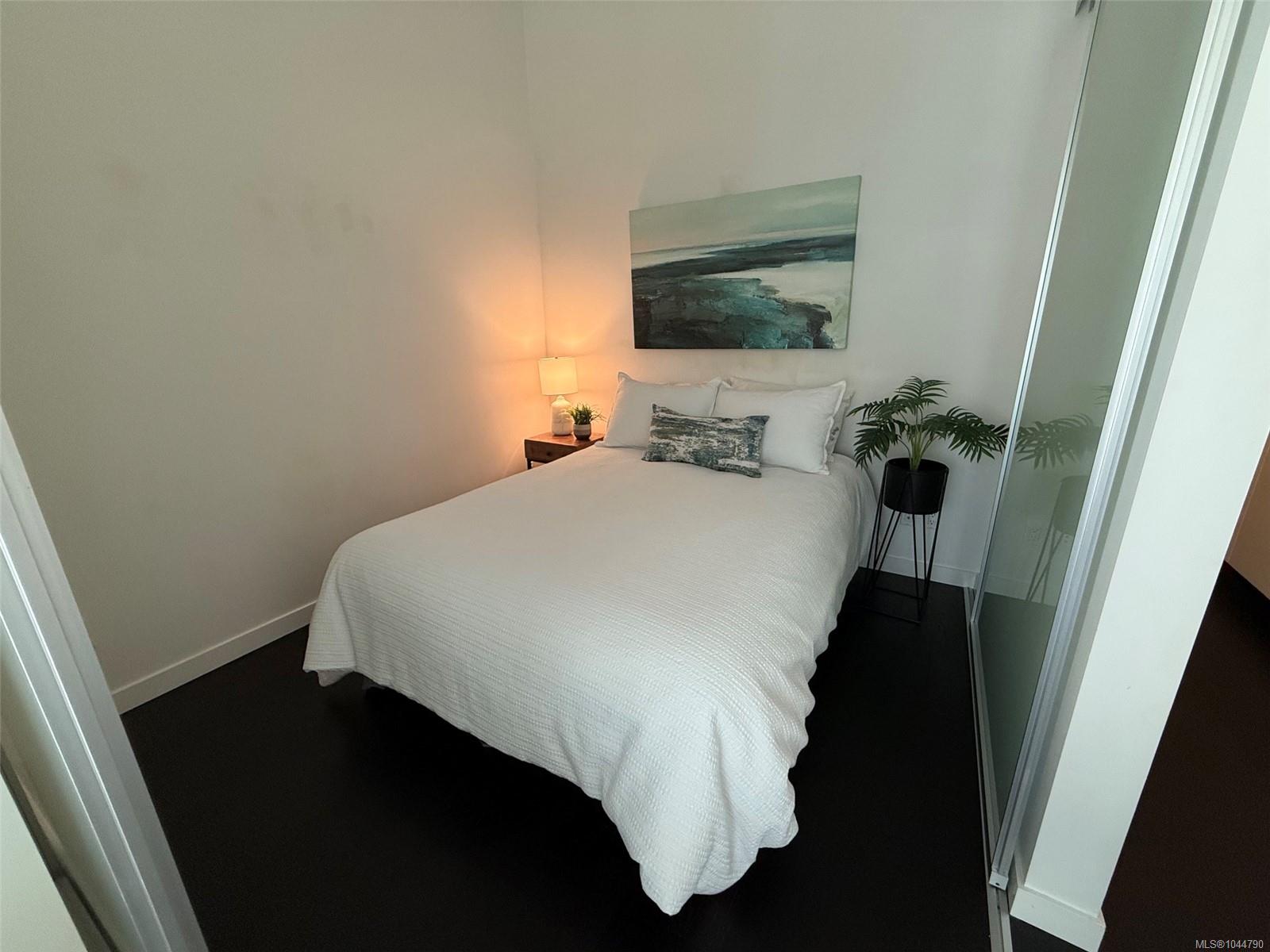 Staged bedroom with a white bed, coastal artwork, bedside lamp, and mirrored closet doors.