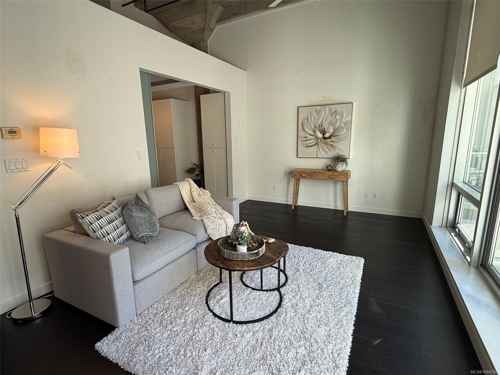 Staged condo living room with gray sofa, round coffee table, white shag rug, and tall windows.