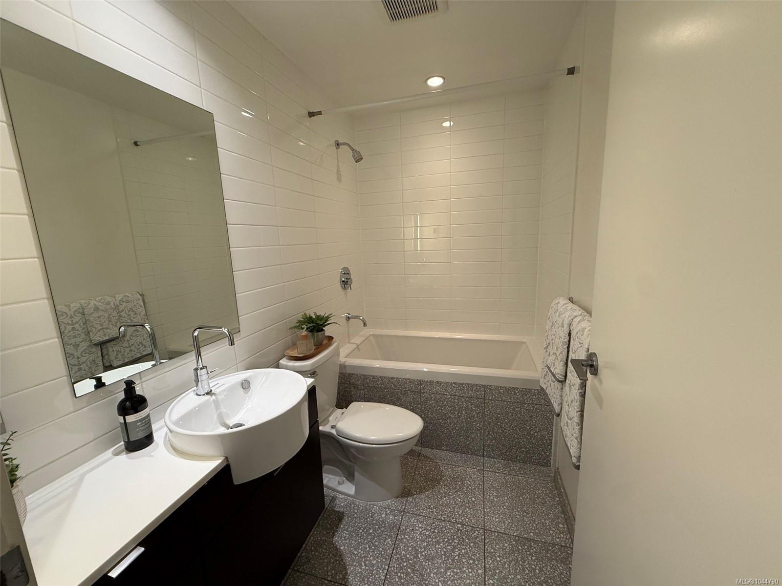 Bathroom with white subway tile, a bathtub and shower, vessel sink, and patterned gray tile.