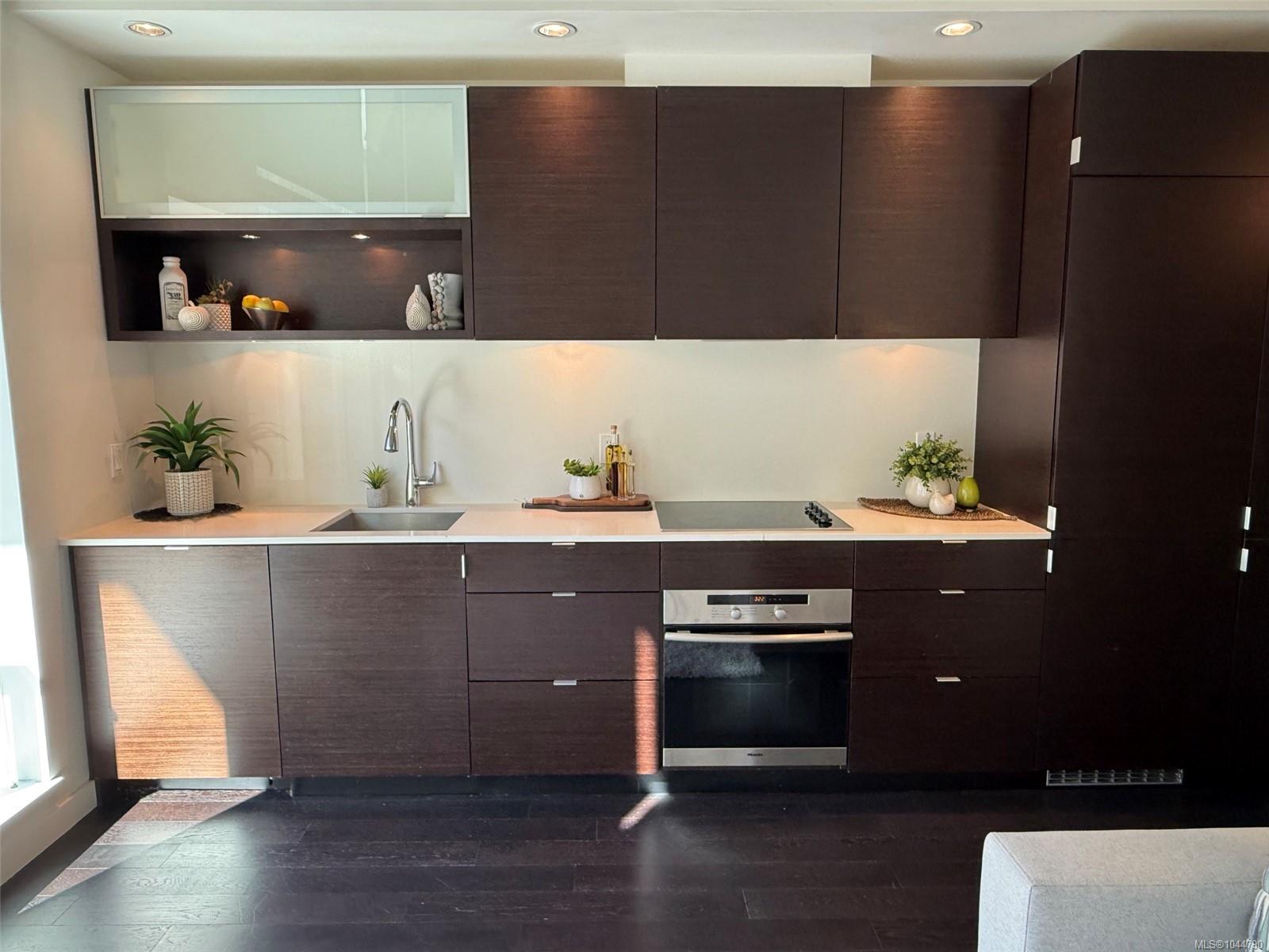Modern kitchen with dark wood cabinets, white counters, and a built-in oven and cooktop.