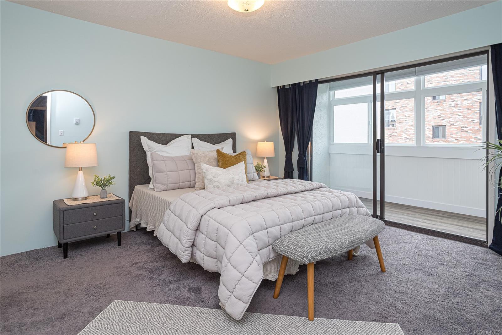 Staged bedroom with a white-quilted bed beside sliding glass doors to an enclosed balcony.