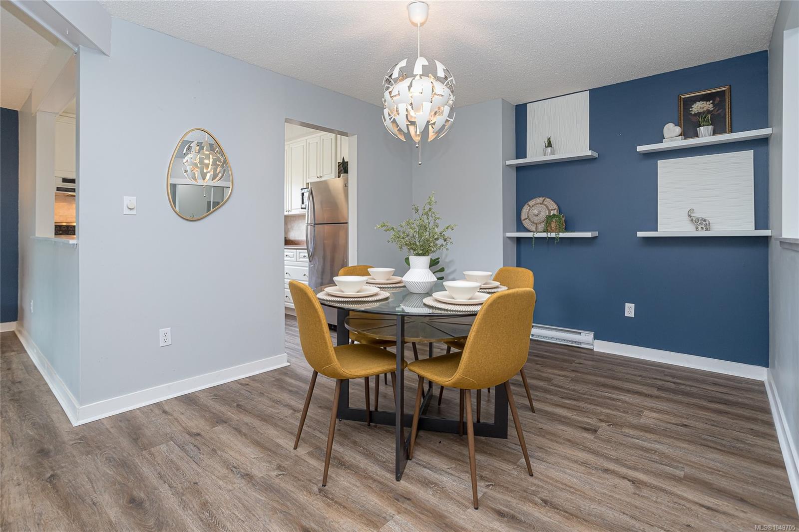 Dining room with a glass-top table, mustard-yellow chairs, and blue accent wall.