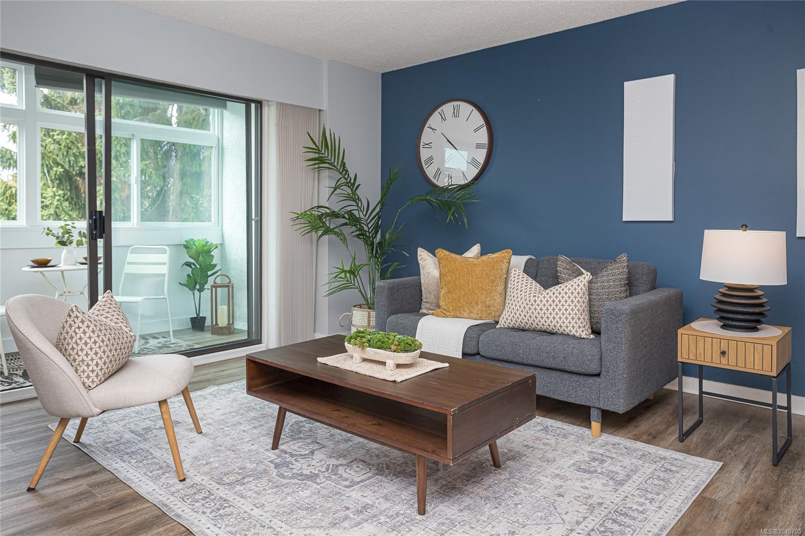 Staged living room with a blue accent wall, gray sofa, and sliding doors to a bright balcony.
