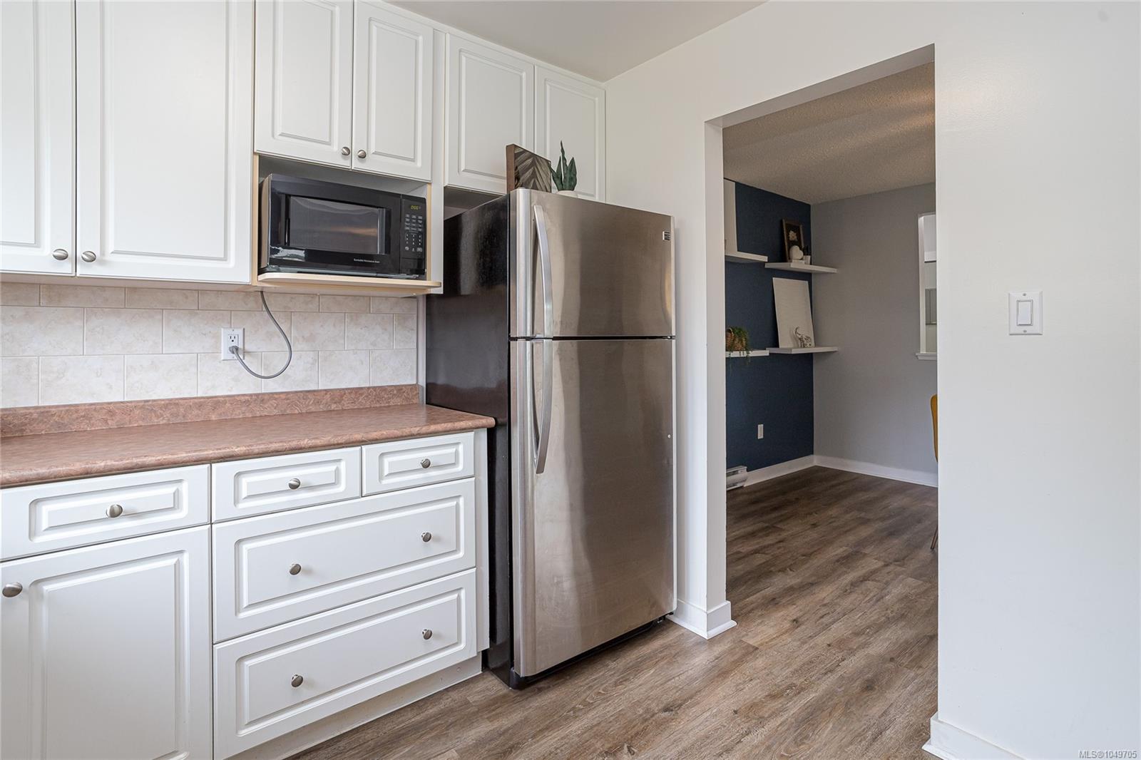 Kitchen with white cabinets, stainless-steel appliances, tile backsplash, and wood-look flooring.
