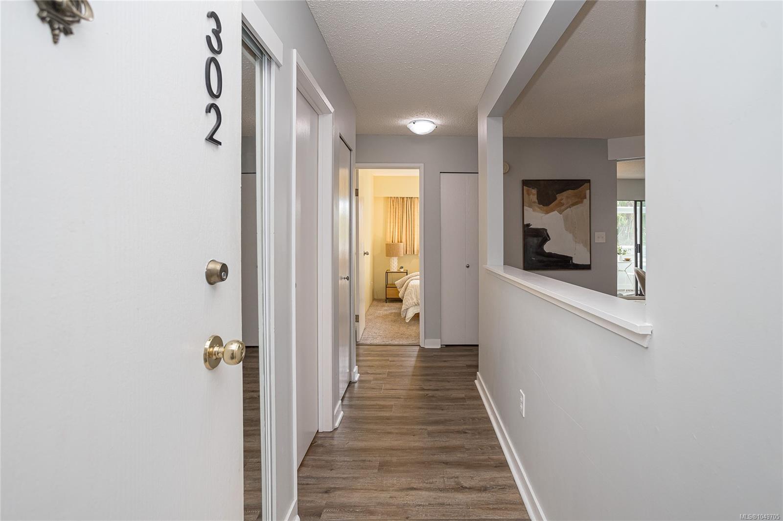 Apartment hallway with dark wood-look floors and a view into a furnished bedroom.