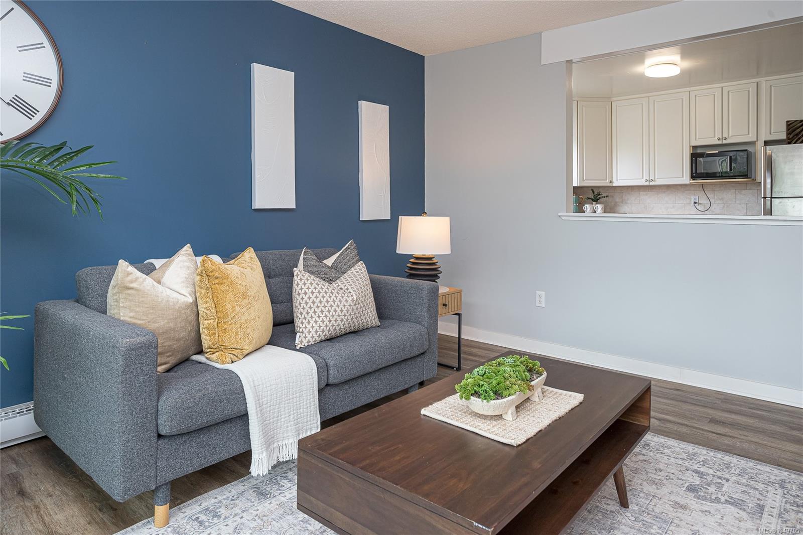 Staged living room with a gray sofa, blue accent wall, and open kitchen.