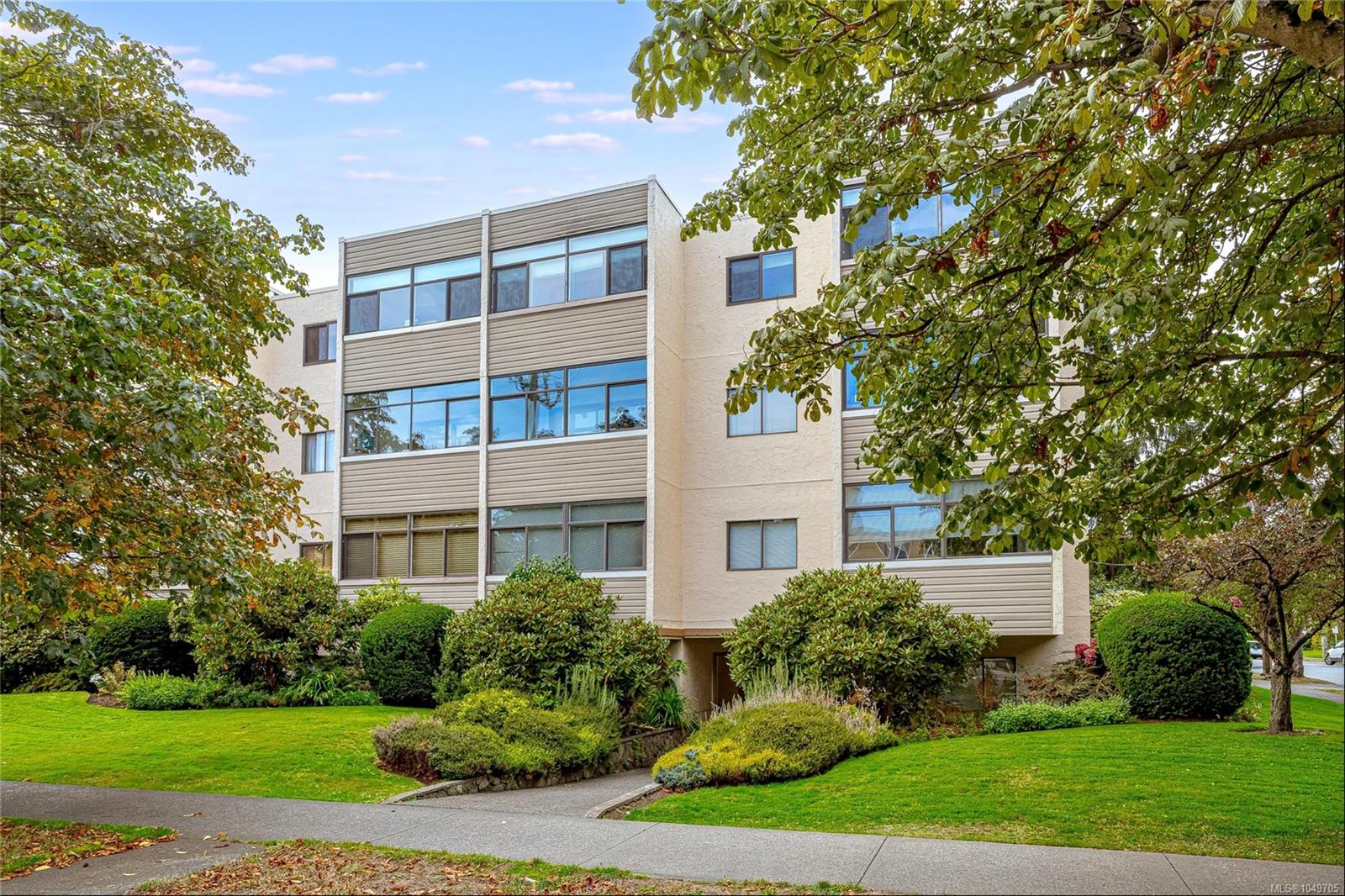Apartment building framed by mature trees, with landscaped grounds and broad windows.