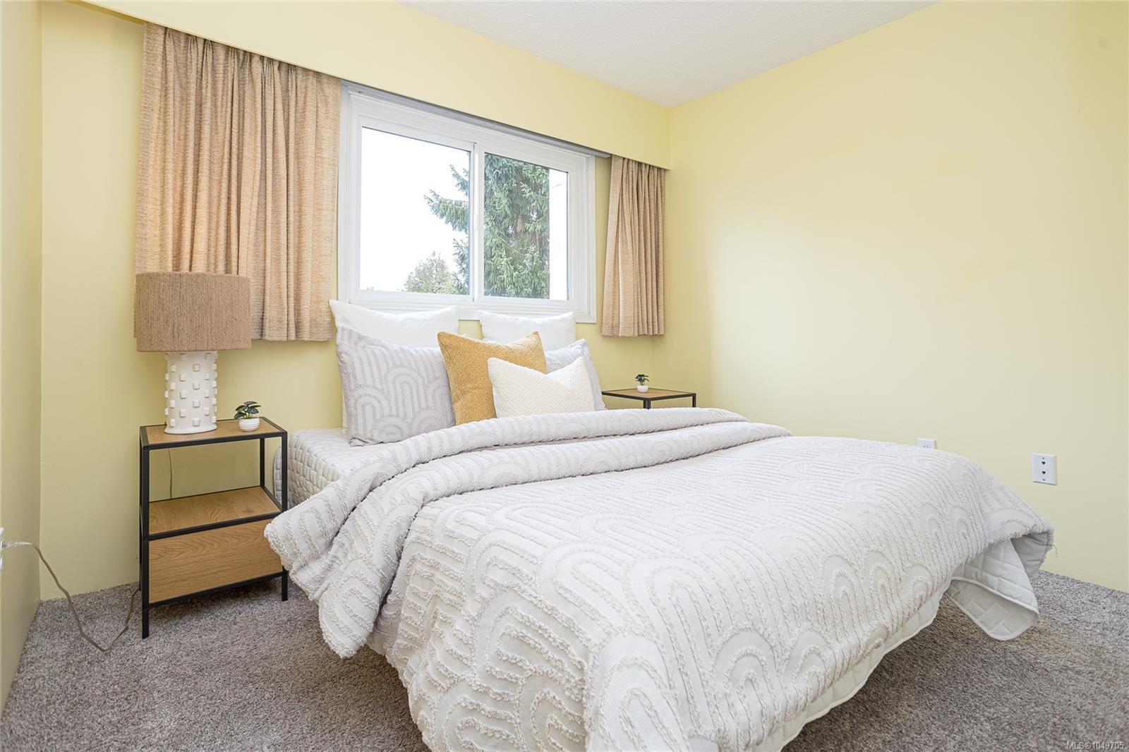 Furnished bedroom with a white textured bed, pale yellow walls, and a window overlooking trees.