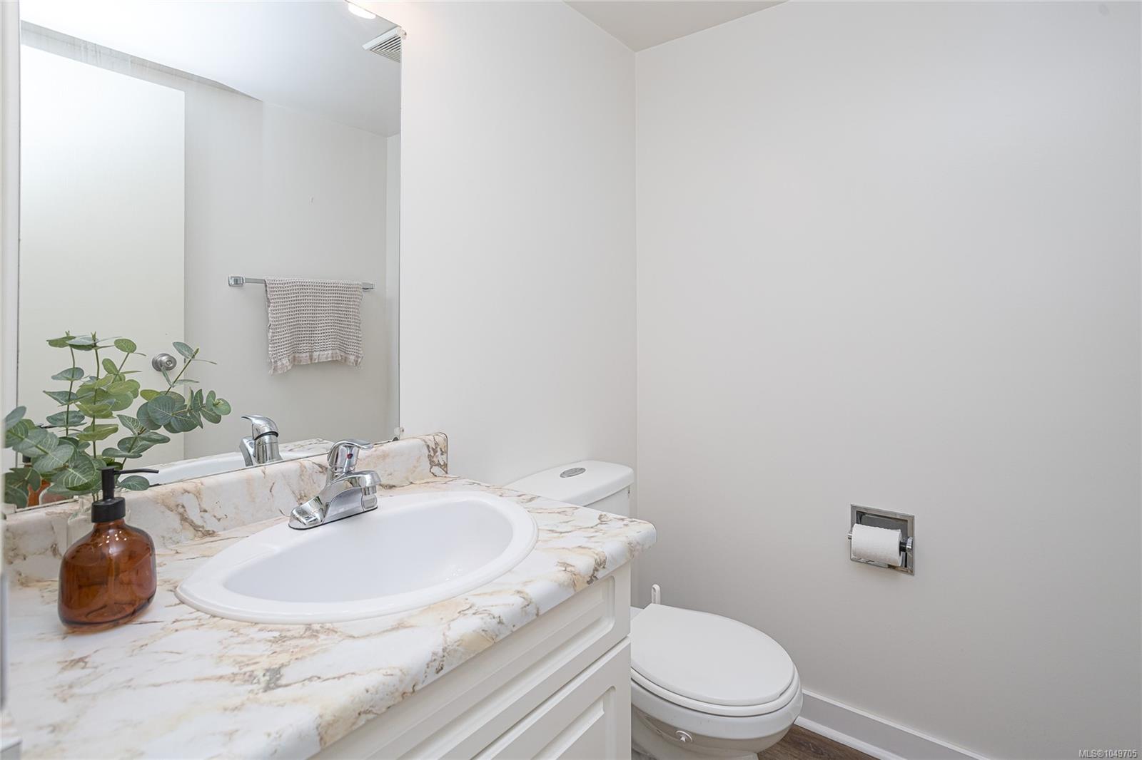 Bathroom vanity with veined stone countertop, large mirror, and toilet.