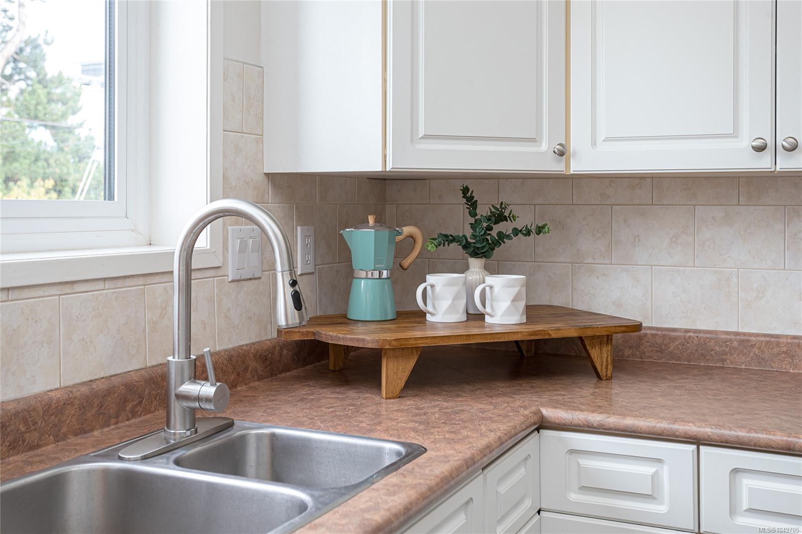 Kitchen sink and countertop with white cabinets, a tiled backsplash, and a turquoise coffee maker.