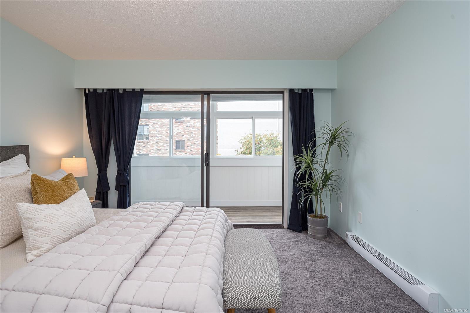 Furnished bedroom with a quilted bed, dark curtains, and sliding glass doors to an enclosed balcony.