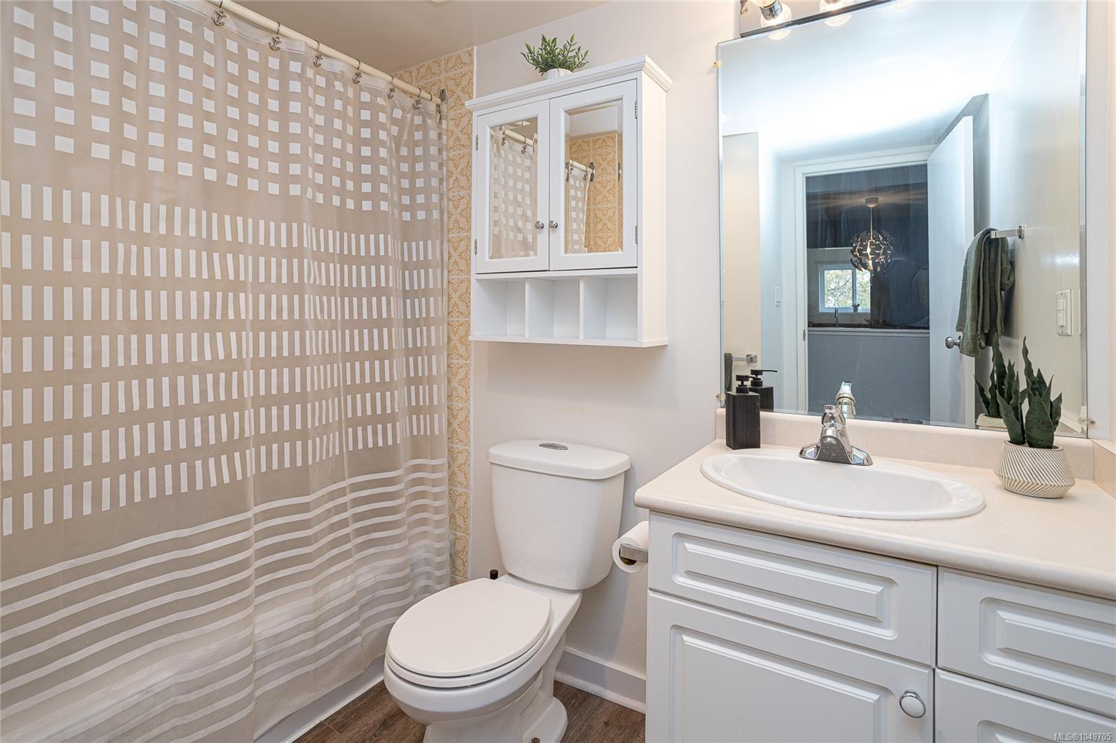 Bathroom with a white vanity and mirrored cabinet beside a beige patterned shower curtain.