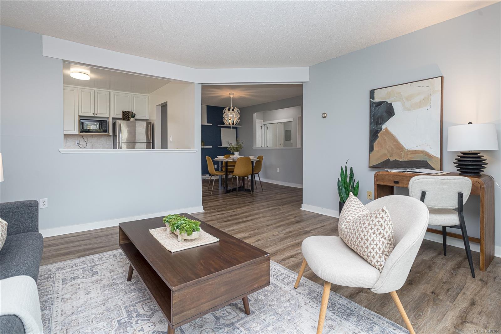 Staged condo living room with a dark coffee table, abstract wall art, and open kitchen and dining area.