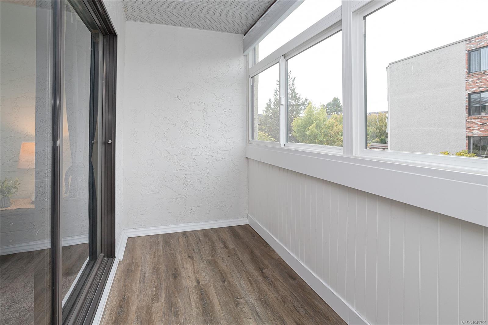 Enclosed balcony with large windows, white paneled walls, and wood-look flooring.