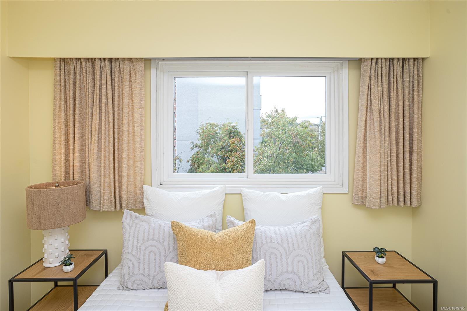 Staged bedroom with a white bed, beige curtains, and a large window.