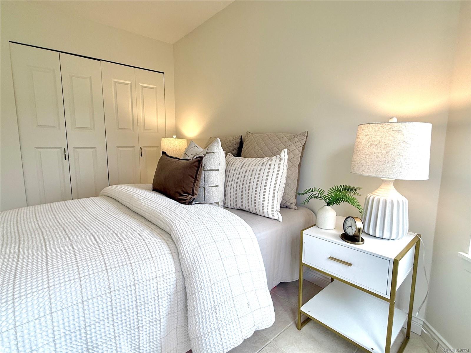 Staged bedroom with a white quilted bed, neutral pillows, paneled closets, and a bedside table.