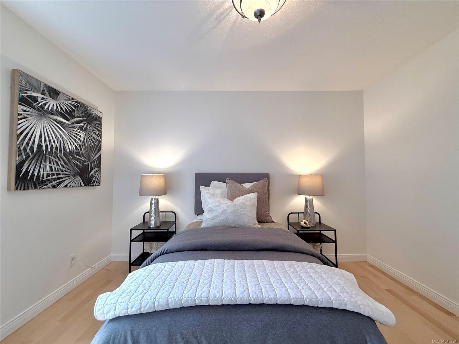 Staged bedroom with a neatly made bed, matching bedside lamps, and framed botanical artwork.