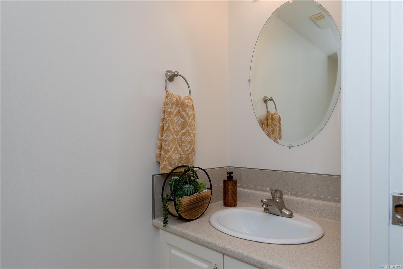 Bathroom vanity with an oval sink, round mirror, and mustard patterned towel.