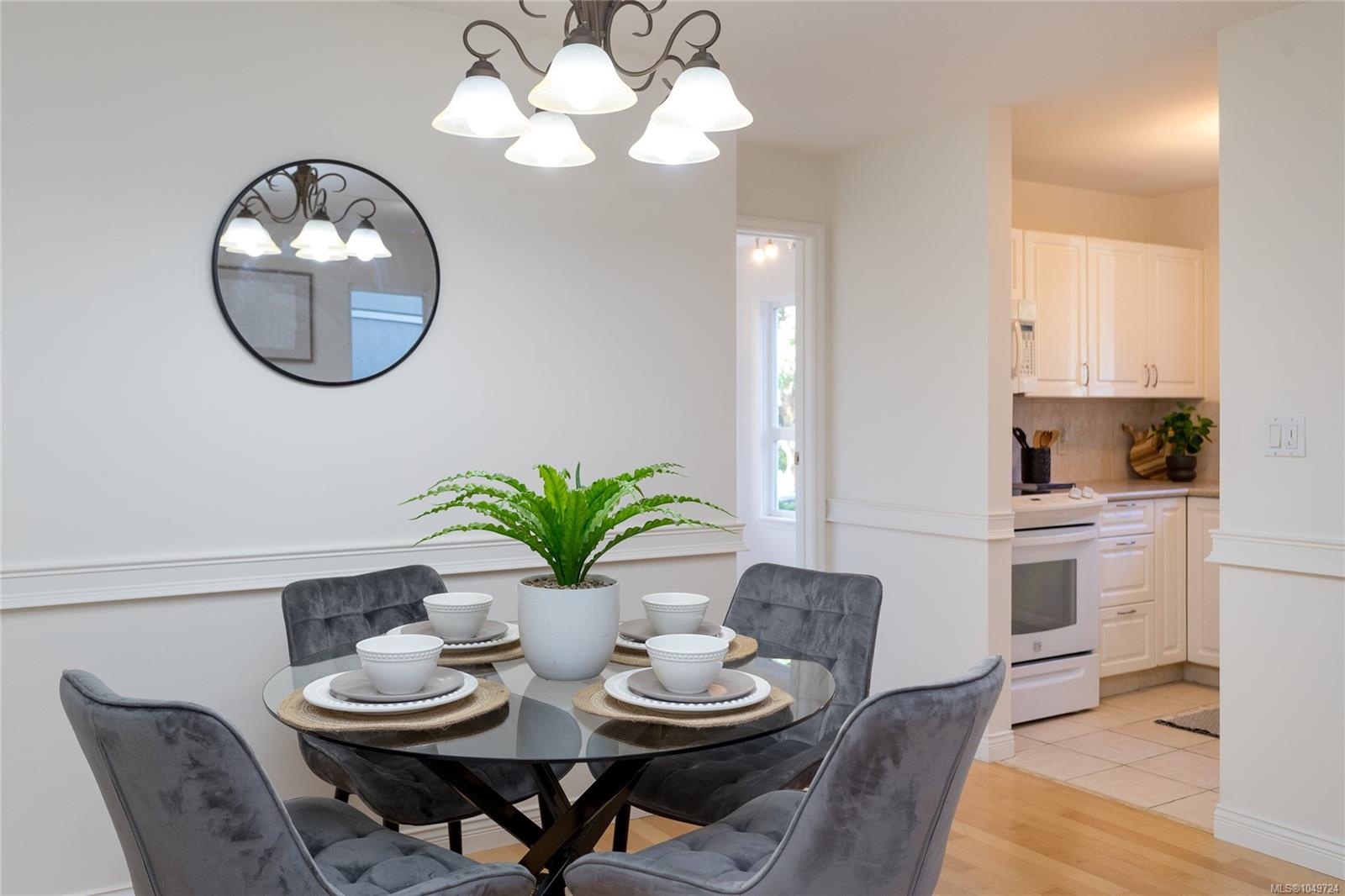 Dining area with a glass table set for four beside a bright white kitchen.