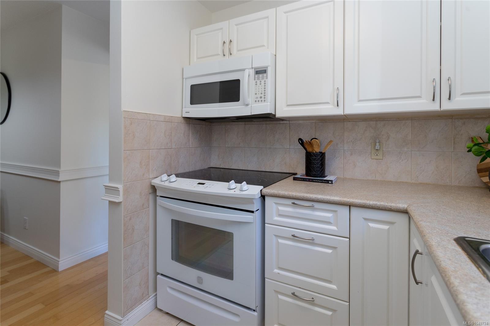 Kitchen with white cabinetry, electric range, microwave, and beige tile backsplash.