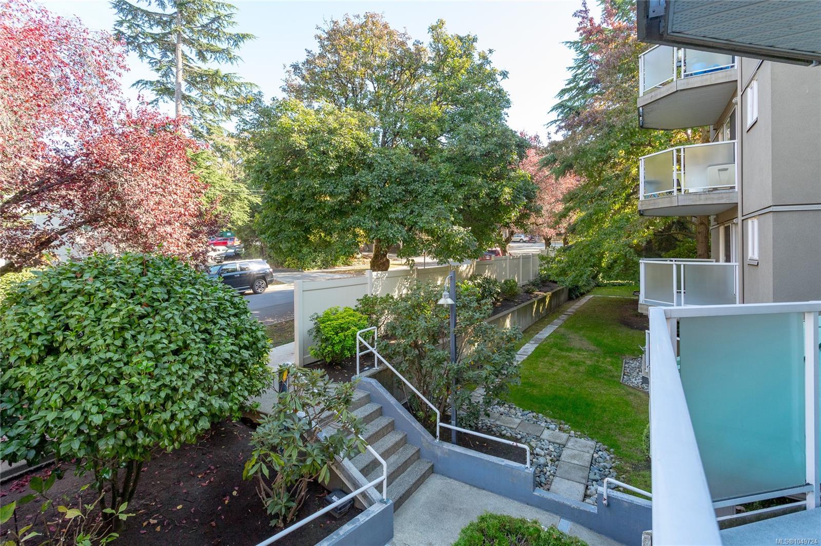 Condominium balconies beside landscaped grounds with stairs and mature autumn trees.