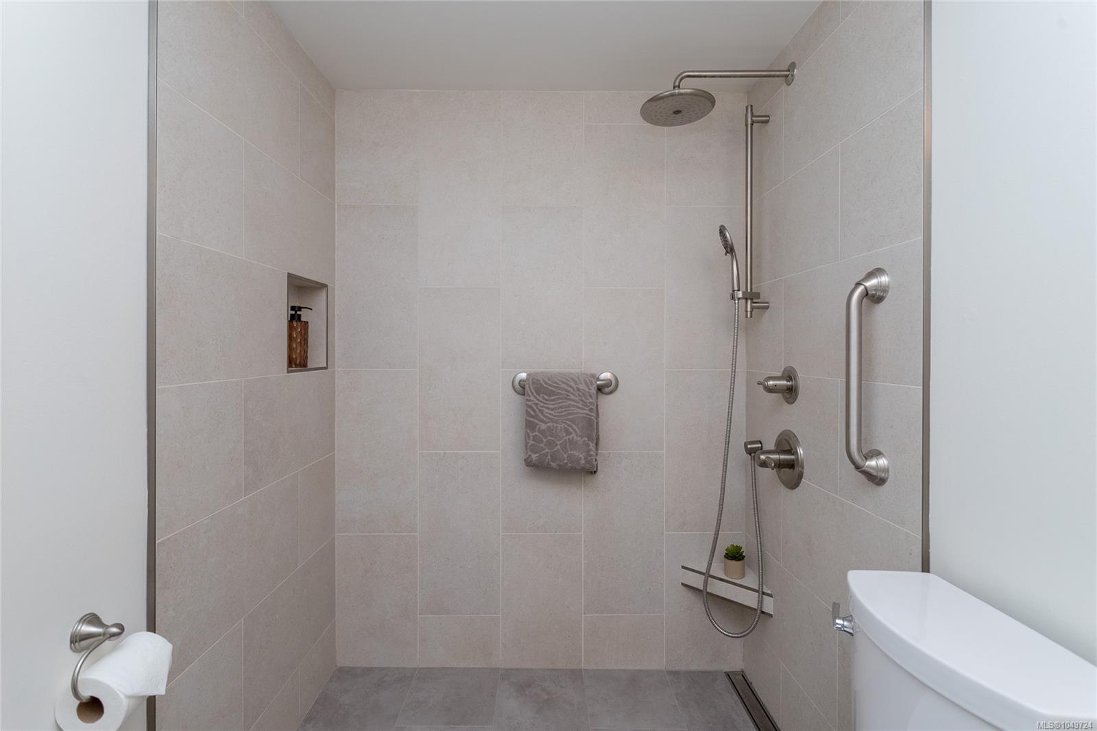 Walk-in tiled shower with rainfall and handheld showerheads, grab bars, and a built-in wall niche.